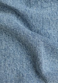 Tejido de mezclilla azul claro con un tejido de sarga. Presenta una superficie suave y texturada con franjas alternas de azul oscuro y claro.