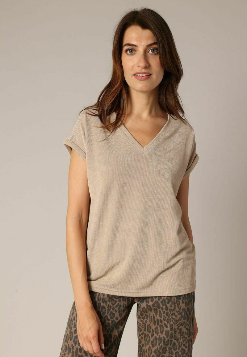 Beige V-hals T-shirt met korte opgerolde mouwen, voorzien van een geribbelde textuur. Gecombineerd met legging met luipaardprint.