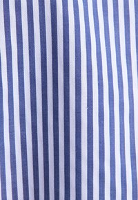 Strisce verticali blu e bianche su tessuto con sottile texture a spina di pesce all'interno delle strisce blu, creando un classico motivo a righe.