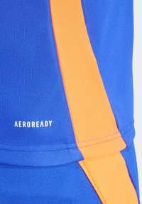 Kék sportos szövet narancssárga oldalsó díszítéssel és fehér "AEROREADY" felirattal. Simaszövet, testhezálló dizájn, ideális aktív öltözethez.