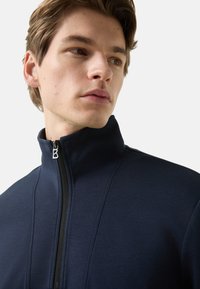 Námořnická bunda se zipem a vysokým límcem, vyrobená z měkké látky. Má stříbrný zip a jemné švy na přední straně.