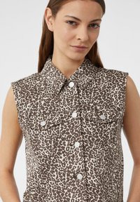 Braunes und elfenbeinfarbenes ärmelloses Denim-Hemd mit Leopardenmuster, Knopfverschluss und Brusttaschen mit Druckknöpfen.