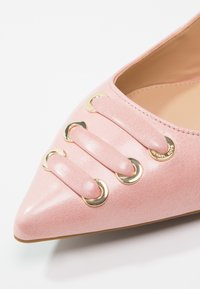 Scarpa rosa con punta a punta e finitura texturizzata, caratterizzata da dettagli in hardware dorato e tre cinturini rosa con anelli dorati che decorano il vamp.