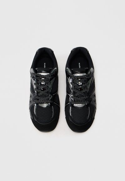 Un par de zapatillas negras de Marc Jacobs con tejido de malla y detalles reflectantes, vistas desde arriba sobre un fondo blanco.