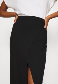 Svart ribbad kjol med en asymmetrisk design och en sidoförslitning. Slät textur, figursydd silhuett, tillsammans med en lös vit topp.