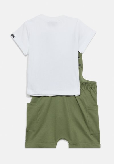 Λευκό κοντομάνικο μπλουζάκι συνδυασμένο με χακί πράσινο κοντό σαλοπέτα με πλαϊνές τσέπες και τιράντες με κουμπιά.