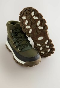 Grüne wasserdichte Wanderschuhe mit strukturierten Gummisohlen, Metallösen und gepolsterten Kragen. Mit einer kontrastierenden weißen Zwischensohle.