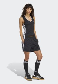 Svart atletisk linnetopp med vita detaljer, matchande svarta shorts och knähöga svarta strumpor med tre vita ränder. Svarta sneakers med gummisulor.