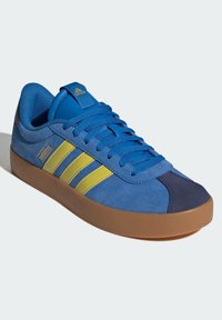 Sneaker blu in pelle scamosciata con strisce gialle, suola in gomma e lacci blu. Presenta una punta rinforzata e una linguetta con marchio.
