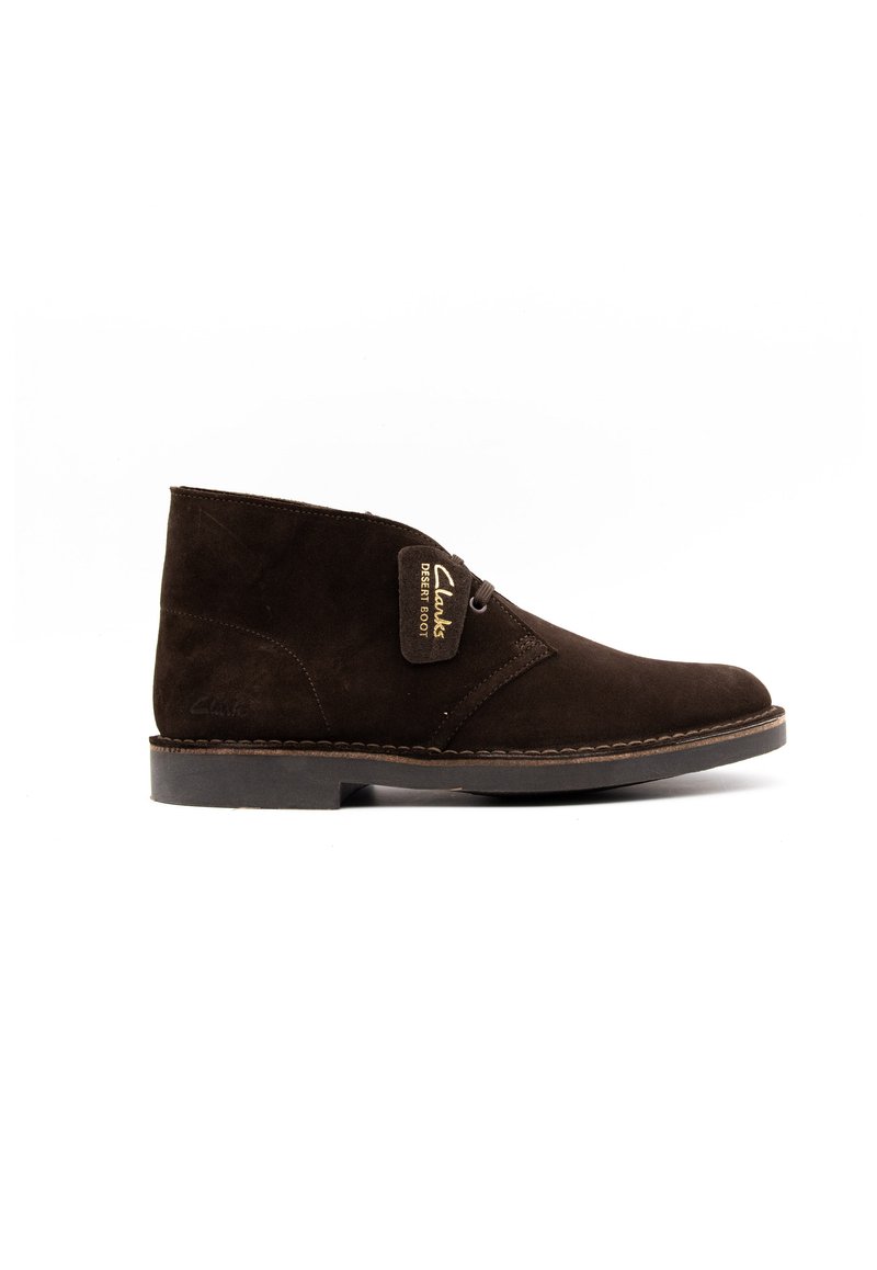 Botín de ante marrón con puntera redonda, que presenta una suela cosida y un diseño con cordones. Incluye una etiqueta de logo dorada con la inscripción "Desert Boot."