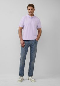 Licht lila polo T-shirt, korte mouwen en kraag. Draagt bij vervaagde blauwe jeans en witte sneakers met beige accenten. Eenvoudig ontwerp.
