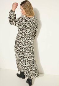 Lange, dierenprint jurk in zwart en crème met een vloeiende ontwerp, lange mouwen, elastische tailleband, en gedragen met zwarte laarzen.