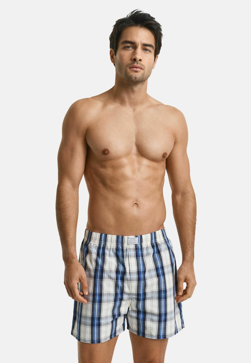 Shorts à carreaux pour homme en bleu, blanc et marine, fabriqués en tissu léger, avec une taille élastique et une étiquette de logo à l'avant.