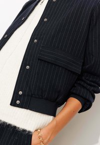 Veste rayée marine avec des fermetures à pression, dotée d'une poche frontale, de poignets côtelés et d'un tricot crème texturé en dessous.