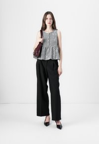 Čierno-biely kockovaný peplum top s okrúhlym výstrihom, kombinovaný s čiernymi širokými nohavicami a čiernymi špicatými podpätkami, drží bordovú tašku.