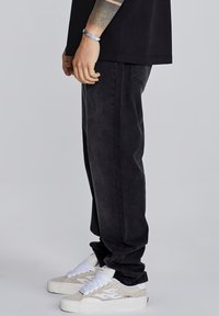 Jeans de denim negro con un diseño de pierna recta, combinados con zapatillas de ante gris claro que tienen detalles y cordones blancos.