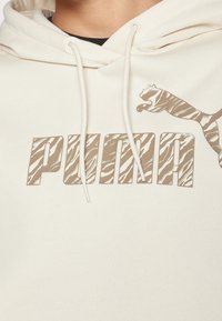 Kremowa bluza z kapturem z dużym logo "PUMA" w beżowym kolorze z wzorem zebry, z trokami i miękką teksturą materiału.