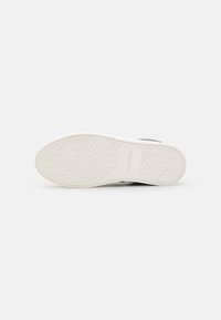 Semelle de chaussure Calvin Klein, en caoutchouc blanc avec une texture circulaire, comportant le nom de la marque embossé, des bords fins et une surface lisse.
