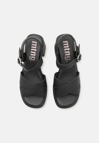 Sorte åpen-tå sandaler med en teksturert kryss-design, ankelstropp med spenne, og en lav blokkhelt. Merkevarelogo synlig på innersålen.