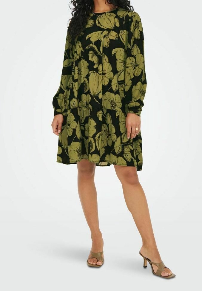 Femme portant une robe noire ample à manches longues avec de grands motifs floraux vert olive, associée à des sandales à talons ouvertes beiges.