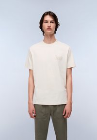 Light beige cotton t-shirt with short sleeves and a crew neckline, featuring a subtle logo print on the left chest area.
