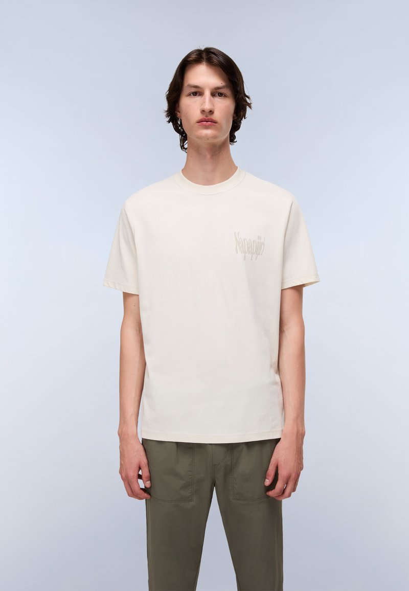 T-shirt en coton beige clair à manches courtes et col rond, avec un imprimé logo subtil sur la partie gauche de la poitrine.