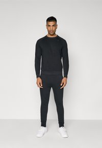 Sort sweatshirt og leggings sæt lavet af blødt materiale. Har lange ærmer, ribbede manchetter og et enkelt design. Kombinationen er med hvide sneakers.