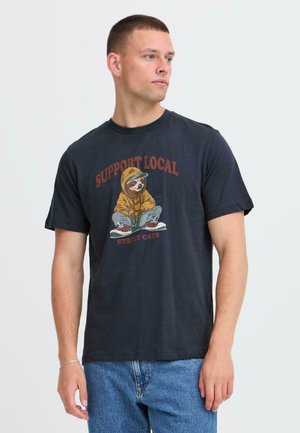 T-shirt en coton noir ornée d'un design graphique d'un paresseux portant un sweat à capuche jaune, avec le texte "SOUTENEZ LES CHATS DE RUE LOCAUX" en rouge.