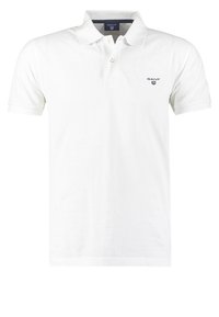 Polo shirt blanc en coton avec un col classique, des manches courtes et un petit logo marine sur la poitrine gauche. Texture lisse.