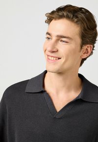 Mörkgrå stickad polo-shirt med V-ringning och kort krage. Texturen är räfflad, vilket framhäver dess avslappnade design.