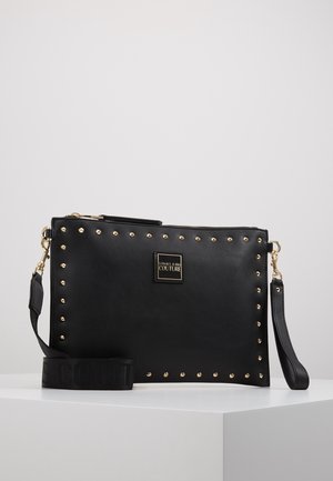 Schwarze rechteckige Clutch mit goldenen Nieten an den Rändern, goldenem Reißverschluss, abnehmbaren Handgelenks- und Schulterriemen und Versace Jeans Couture Logo-Plakette.