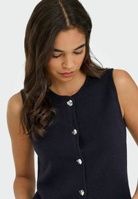 Dunkel gestricktes ärmelloses Top mit rundem Ausschnitt, das vorne mit fünf silberfarbenen Knöpfen verziert ist. Weicher Stoff und taillierte Passform.