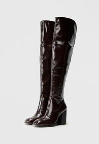 Burgundowe skórzane kozaki za kolano o gładkiej fakturze, zaokrąglonym nosku i grubym obcasie typu blok, wyróżniające się minimalistycznym wzornictwem i widocznym przeszyciem.