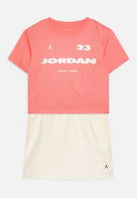 Camiseta corta de manga con estampado coral y texto y logotipo en blanco "JORDAN". Combinada con una falda cremosa que presenta bolsillos laterales y un acento de logotipo.