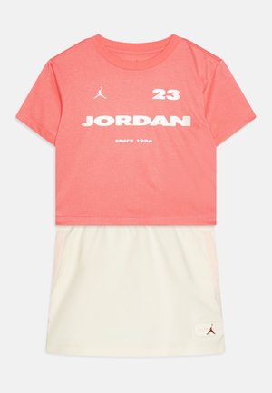 Koraļļu krāsas T-krekls ar īsām piedurknēm, uz tā balts "JORDAN" uzraksts un logo. Apvienots ar krēmkrāsas svārkiem, kuriem ir sānu kabatas un logo akcents.