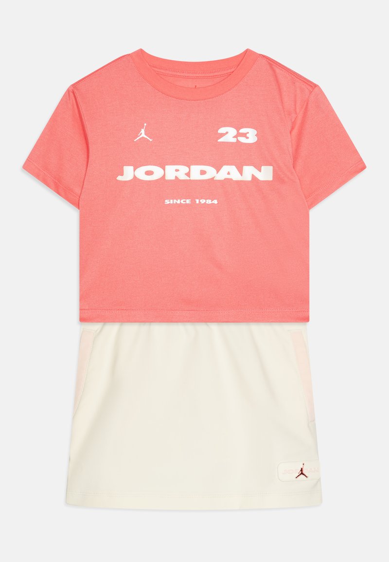 Koralo spalvos trumpas rankovėmis marškinėliai su baltais „JORDAN“ užrašu ir logotipu. Suderinti su kreminės spalvos sijonu, turinčiu šonines kišenes ir logotipo akcentą.