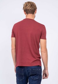 T-shirt à manches courtes marron en coton, avec un col ras du cou et un design simple, associé à un jean bleu foncé.