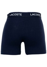 Granatowe bawełniane bokserki z białym logo Lacoste na pasku. Charakteryzują się dopasowanym krojem i prostymi nogawkami, z gładką teksturą.