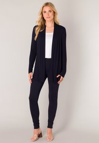 Marineblauwe open voorkardigan met lange mouwen, gecombineerd met een wit topje en bijpassende legging. De outfit heeft een gladde, lichtgewicht stof en een minimalistisch ontwerp.