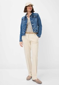 Giubbotto di jeans, camicia a righe bianche e blu, pantaloni avorio, cintura beige e scarpe morbide. Outfit casual con dettagli di bottoni e tasche.