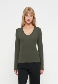 Langarmige, olijfgroene top met een geribbelde textuur, ronde halslijn en een aansluitend ontwerp, gecombineerd met hoogoplopende zwarte broek.