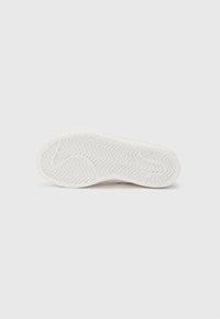 Semelle de basket blanche avec un motif en chevrons texturé, forme arrondie et bord plat. Matériau durable avec des rainures discrètes pour assurer une bonne adhérence.