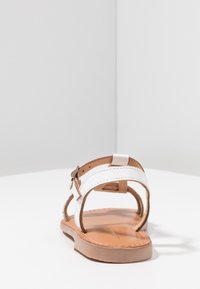 Sandalia blanca con un diseño de respaldo abierto, correas de cuero, cierre de hebilla ajustable y una suela marrón lisa. Estilo simple y minimalista.