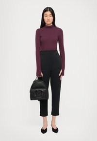 Schwarzer Leder-Rucksack mit goldenen Logodetails, getragen mit einem enganliegenden burgunderfarbenen Rollkragenpullover und maßgeschneiderten schwarzen Hosen. Texturiertes Gewebe und strukturierte Form.