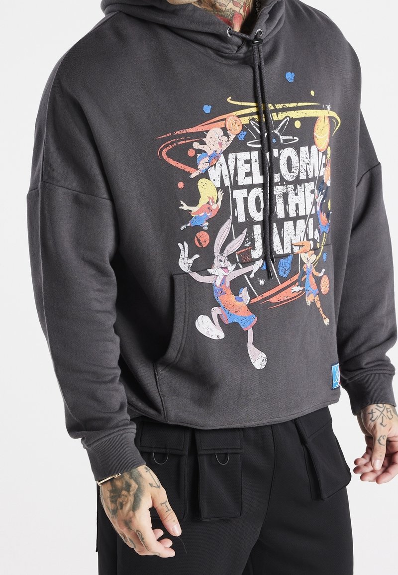 Sudadera gris con un estampado gráfico que presenta personajes de dibujos animados y el texto "BIENVENIDO AL JAM". Tiene un bolsillo frontal y capucha ajustable.