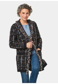 Strick-Cardigan in Schwarz, Blau und Orange mit strukturiertem Muster, übergroßer Kapuze und offenem Design, kombiniert mit Jeans.