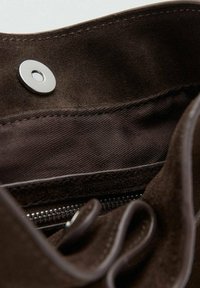 Interior de bolso de ante marrón con cierre a presión plateado y detalle de cremallera. Textura suave con un acabado blando y bordes bien cosidos.
