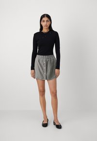 Haut noir à manches longues avec un design asymétrique et des détails de boutons, associé à une jupe rayée dotée d'un bouton sur le devant et d'une taille élastique.
