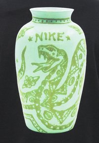 Zaļš vāze ar izsmalcinātu čūskas dizainu, ziedu akcentiem un vārdu "NIKE" virs čūskas galvas uz gaiša fona.