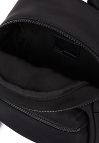 Black fabric bag with visible open zipper revealing an empty interior pocket and a stitched leather label inside.